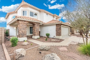 A two-story house with a stone facade, a tiled roof, and a front yard with landscaping. - Fairway Oasis:  Arrowhead Ranch Fairway Retreat with Private Pool (Glendale)