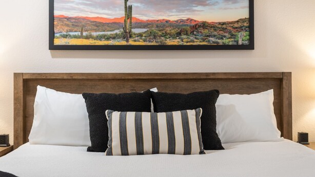 A bed with white bedding and two pillows, one striped and one solid black, against a wooden headboard. - Fairway Oasis:  Arrowhead Ranch Fairway Retreat with Private Pool (Glendale)