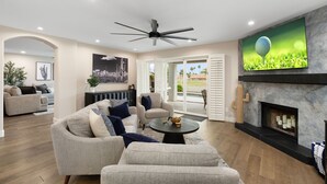 A spacious living room with a fireplace, a ceiling fan, and a television mounted on the wall. - Fairway Oasis:  Arrowhead Ranch Fairway Retreat with Private Pool (Glendale)