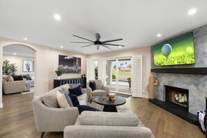 A spacious living room with a fireplace, a ceiling fan, and a television mounted on the wall. - Fairway Oasis:  Arrowhead Ranch Fairway Retreat with Private Pool (Glendale)