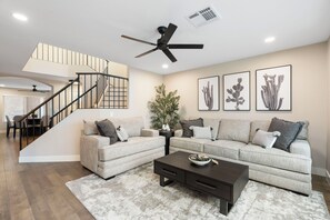 A living room with a staircase, a ceiling fan, a coffee table, and a large plant. - Fairway Oasis:  Arrowhead Ranch Fairway Retreat with Private Pool (Glendale)