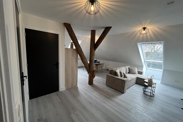 A spacious loft with a high ceiling, exposed wooden beams, a large window, and a cozy seating area.