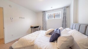 Ein Schlafzimmer mit einem Bett, Kissen, einem Schreibtisch und einem Fenster mit Vorhängen.