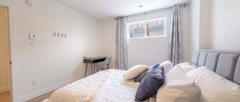Un dormitorio con cama, almohadas, escritorio y ventana con cortinas.