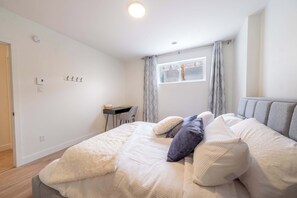 Quarto com cama, almofadas, escrivaninha e janela com cortinas.