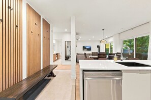 A modern kitchen with a built-in dishwasher, wooden paneling on the left, and a dining area with a view of greenery.