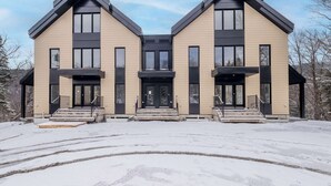 Ein modernes, zweistöckiges Haus mit einer symmetrischen Fassade, großen Fenstern und einem zentralen Eingang mit Stufen.