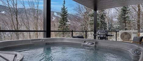 A hot tub with a view of snow-covered trees and mountains.