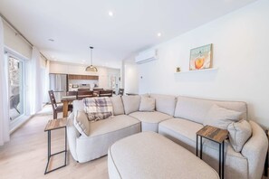 A modern living room with a sectional sofa, a dining area with a table and chairs, and a kitchen in the background.