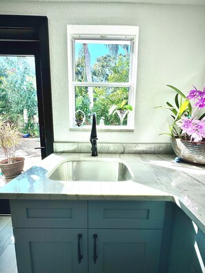 A kitchen with a sink, cabinets, and a window overlooking a garden. - Luxurious upscale guest suite with private entrance and private tropical garden. (Gulfport)