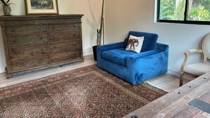 A room with a blue sofa, a wooden dresser, a patterned rug, and a window with a view of greenery. - Luxurious upscale guest suite with private entrance and private tropical garden. (Gulfport)