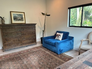 A room with a blue sofa, a wooden dresser, a patterned rug, and a window with a view of greenery. - Luxurious upscale guest suite with private entrance and private tropical garden. (Gulfport)