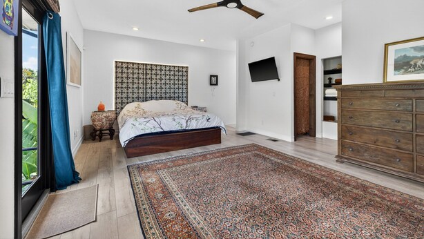 A bedroom with a bed, a wooden dresser, a patterned rug, a ceiling fan, and a TV mounted on the wall. - Luxurious upscale guest suite with private entrance and private tropical garden. (Gulfport)