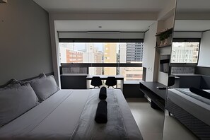 A modern hotel room with a large bed, a desk, and a view of the cityscape. - VN Oscar Freire (São Paulo)