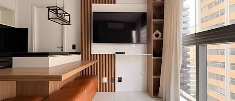 A modern kitchen with a built-in TV, wooden bar counter, and a large window with a city view.