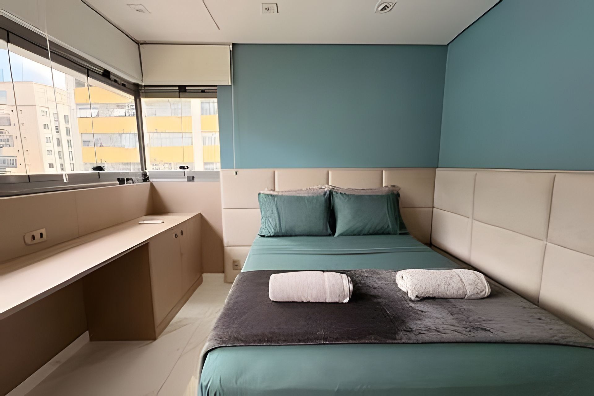 A modern bedroom with a bed, a desk, and a window overlooking a cityscape.