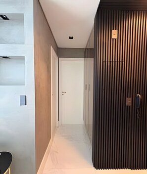 A hallway with a white door at the end, a dark wooden panel wall, and a light-colored floor. - VN Oscar Freire (São Paulo)