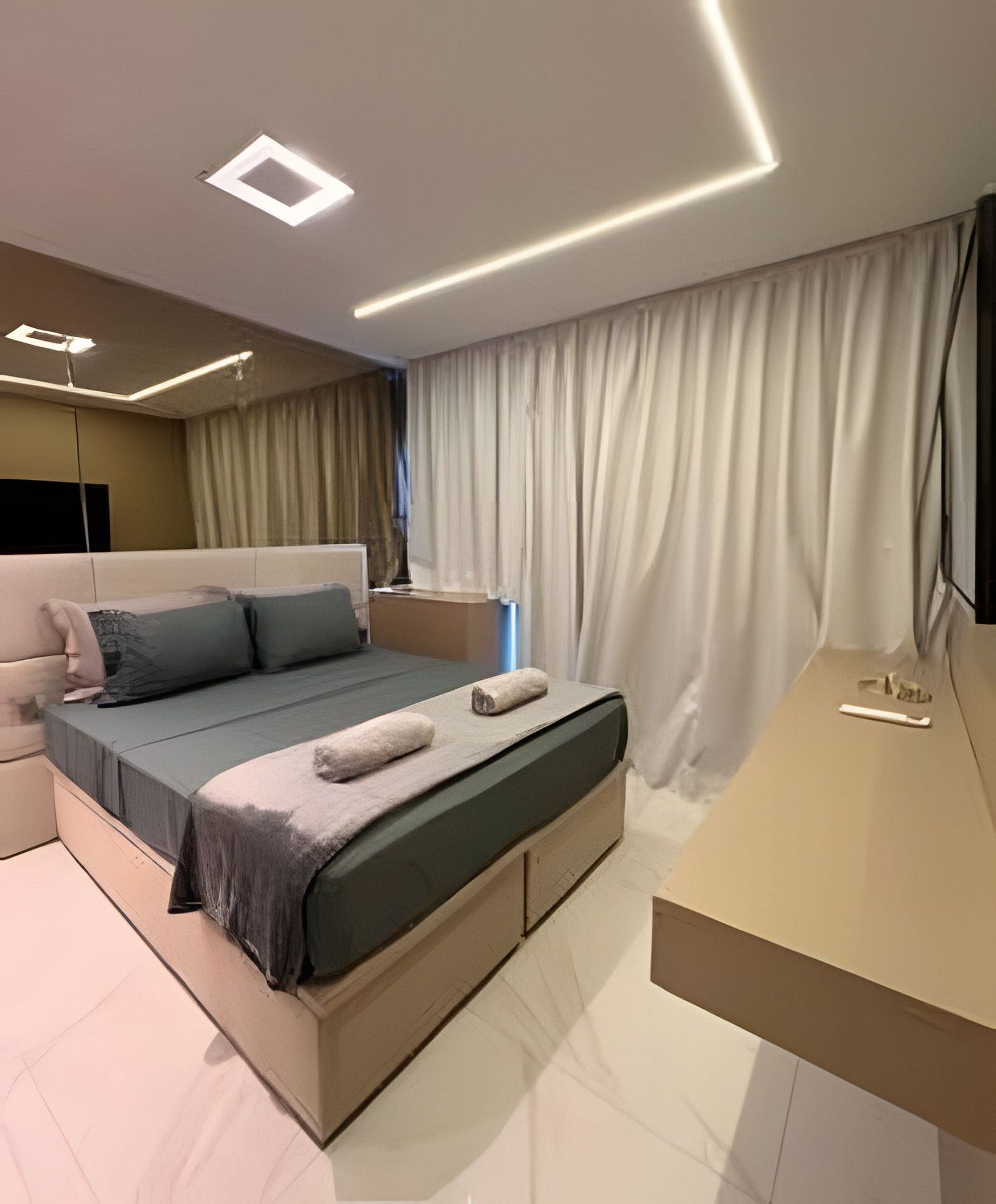 Een moderne slaapkamer met een bed, nachtkastje en een groot raam met gordijnen.