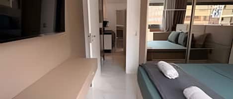 A hotel room with a bed, a TV, a desk, and a sliding door leading to a balcony.