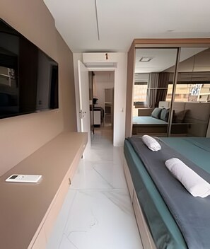 Habitación de hotel con cama, televisor, escritorio y puerta corrediza que da a un balcón.