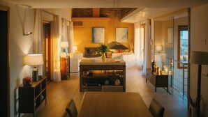 Una sala moderna con una mesa de comedor de madera, un sofá y un televisor. Hay cortinas, una lámpara y un florero con flores.