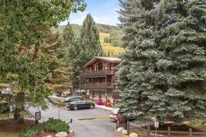 Un chalet avec une façade en bois, un balcon et un espace de stationnement où sont garées des voitures.