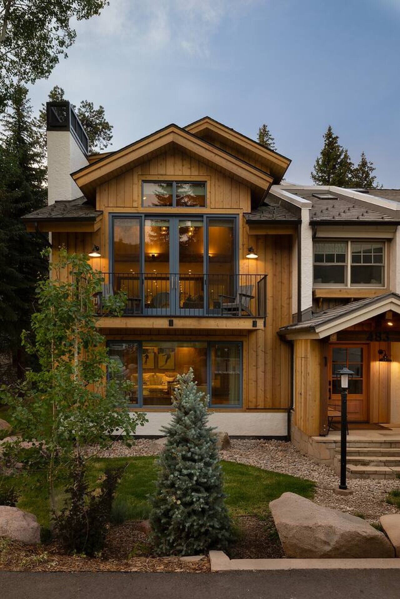 A two-story wooden house with a balcony, large windows, and a small Christmas tree in the front yard.