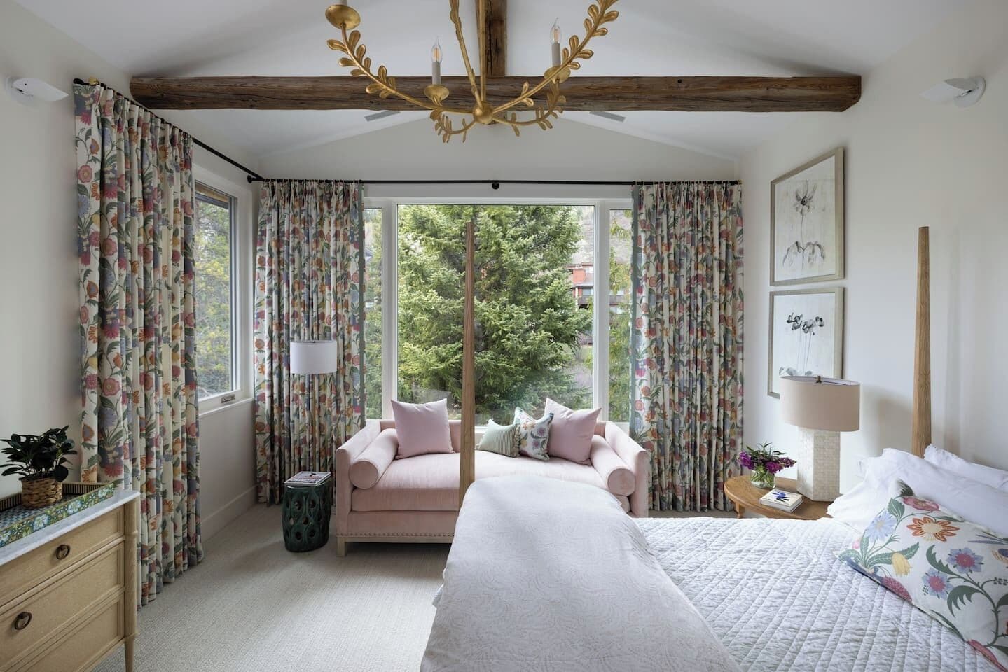 A bedroom with a bed, a sofa, a window with curtains, a chandelier, and artwork on the wall.