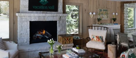 A cozy living room with a fireplace, a chandelier, and a sign reading 'vacation vaill'.
