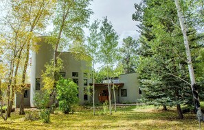A modern building with a flat roof, surrounded by a variety of trees and a grassy area.