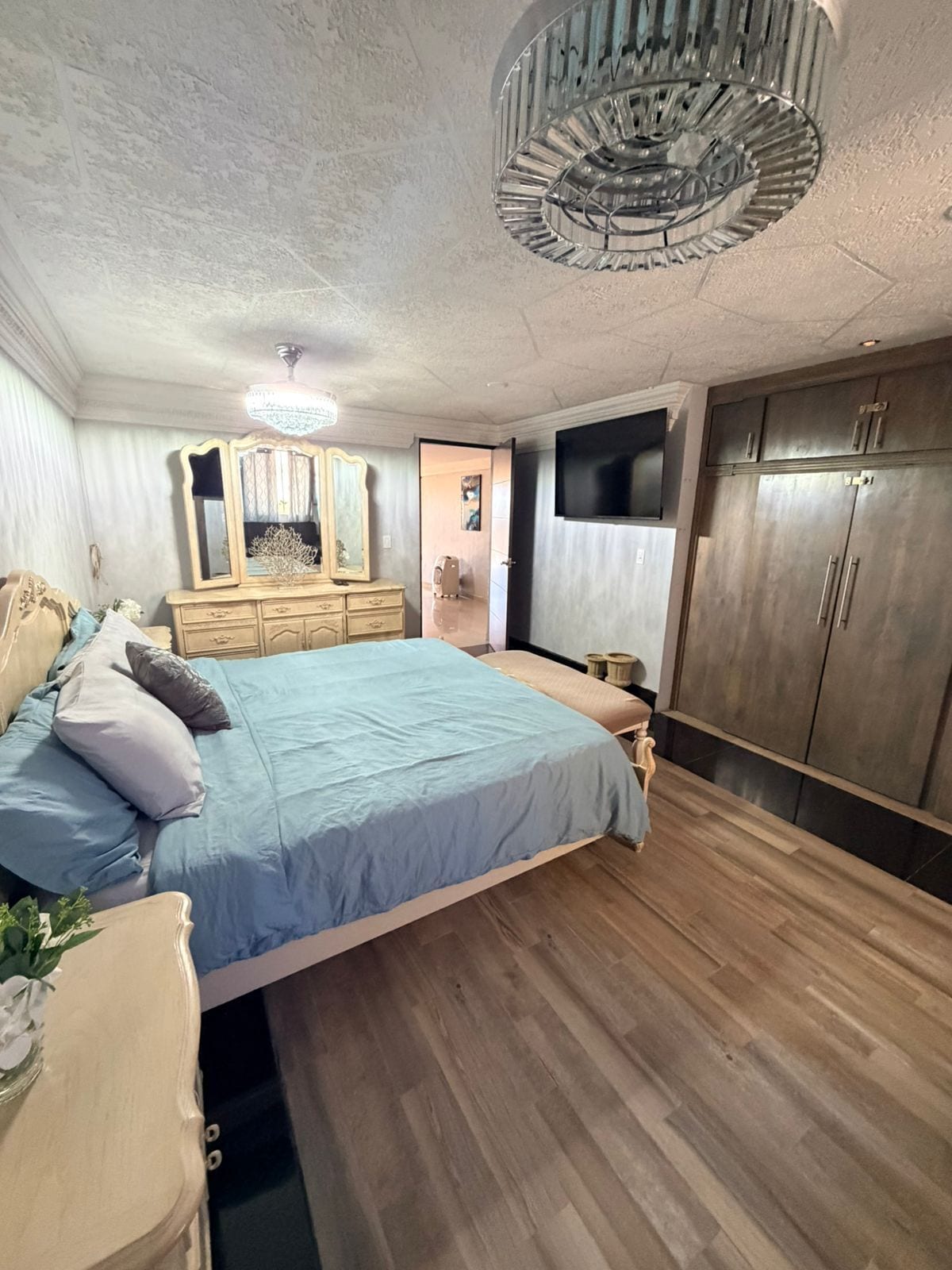 Ein Schlafzimmer mit Bett, Schminktisch, Spiegel, Kleiderschrank und einer Chandelüster.