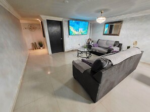 A modern living room with a grey sectional sofa, a glass coffee table, and a large flat-screen TV mounted on the wall. - Casa renovada,espaciosa y segura con lavadora y secadora. Facturamos (Heroica Ciudad de Cananea)