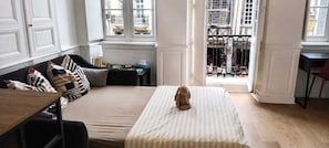 Ein Zimmer mit einem Bett, einem Sofa, einem kleinen Tisch und einem Fenster mit Blick auf Gebäude.