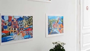 Ein Essbereich mit einem Holztisch und einer Bank, drei farbenfrohe Bilder an der Wand und ein Blumentopf auf dem Tisch.