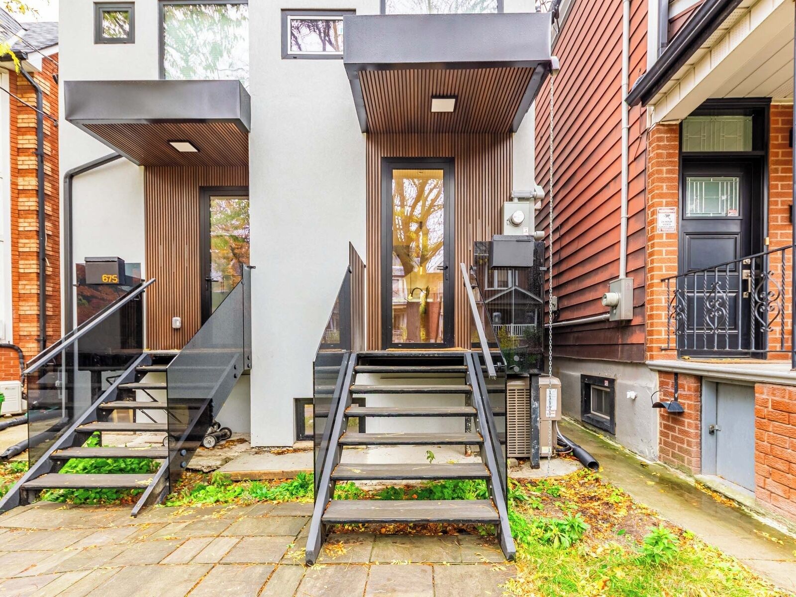 A modern building with a staircase leading to a door, a small outdoor area with steps, and a brick wall.