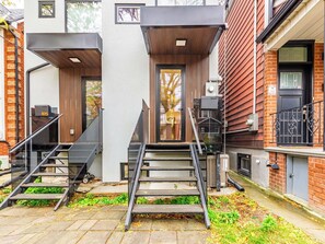 A modern building with a staircase leading to a door, a small outdoor area with steps, and a brick wall. - Luxury 3BR Toronto Home | Little Italy & Bloor West | Parking (Toronto)
