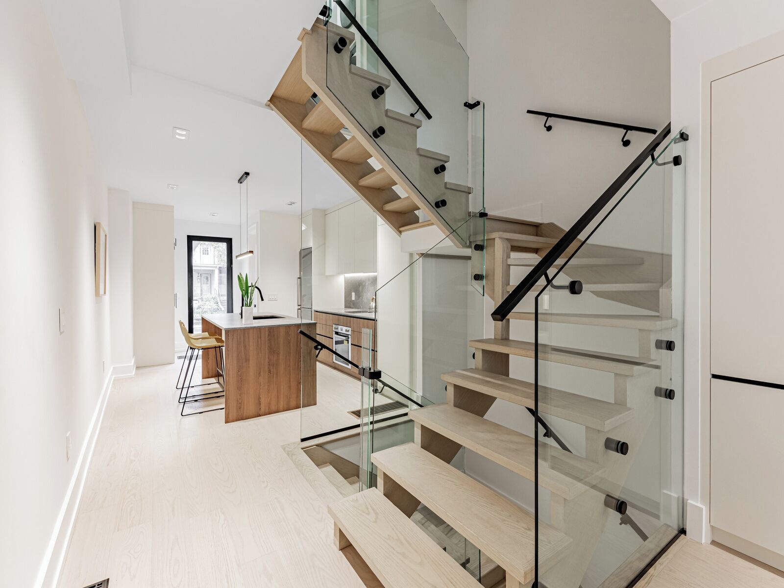A modern interior with a glass staircase, wooden flooring, and a kitchen area.