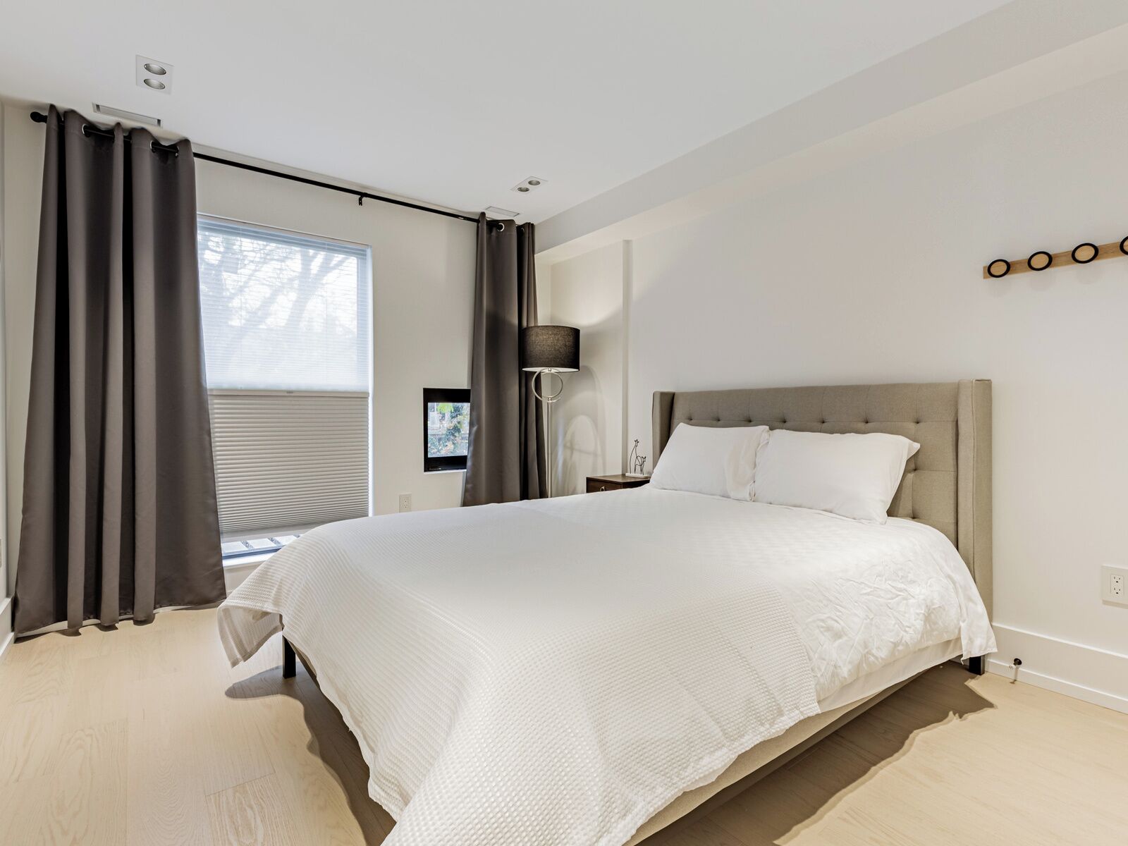 A modern bedroom with a large bed, a bedside table, a lamp, and a view of the outdoors.