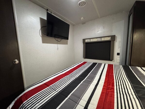 A bedroom with a bed, a television mounted on the wall, and a window with a blind.