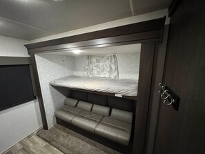 A compact room with a bunk bed, a small seating area, and a flat-screen TV.
