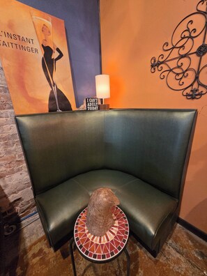 A corner seating area with a cushioned bench, a small table with a decorative item, a wall-mounted lamp, and a poster with text and a silhouette.