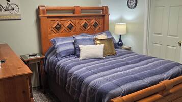 A bedroom with a wooden headboard, a bed with a blue and purple striped bedspread, a nightstand with a lamp, a wooden dresser, and a rug on the floor.