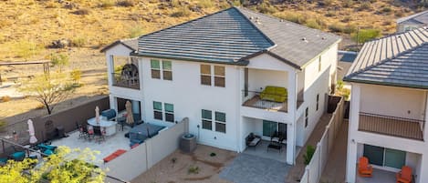 A two-story house with a patio, outdoor seating, and a view of a mountainous landscape.