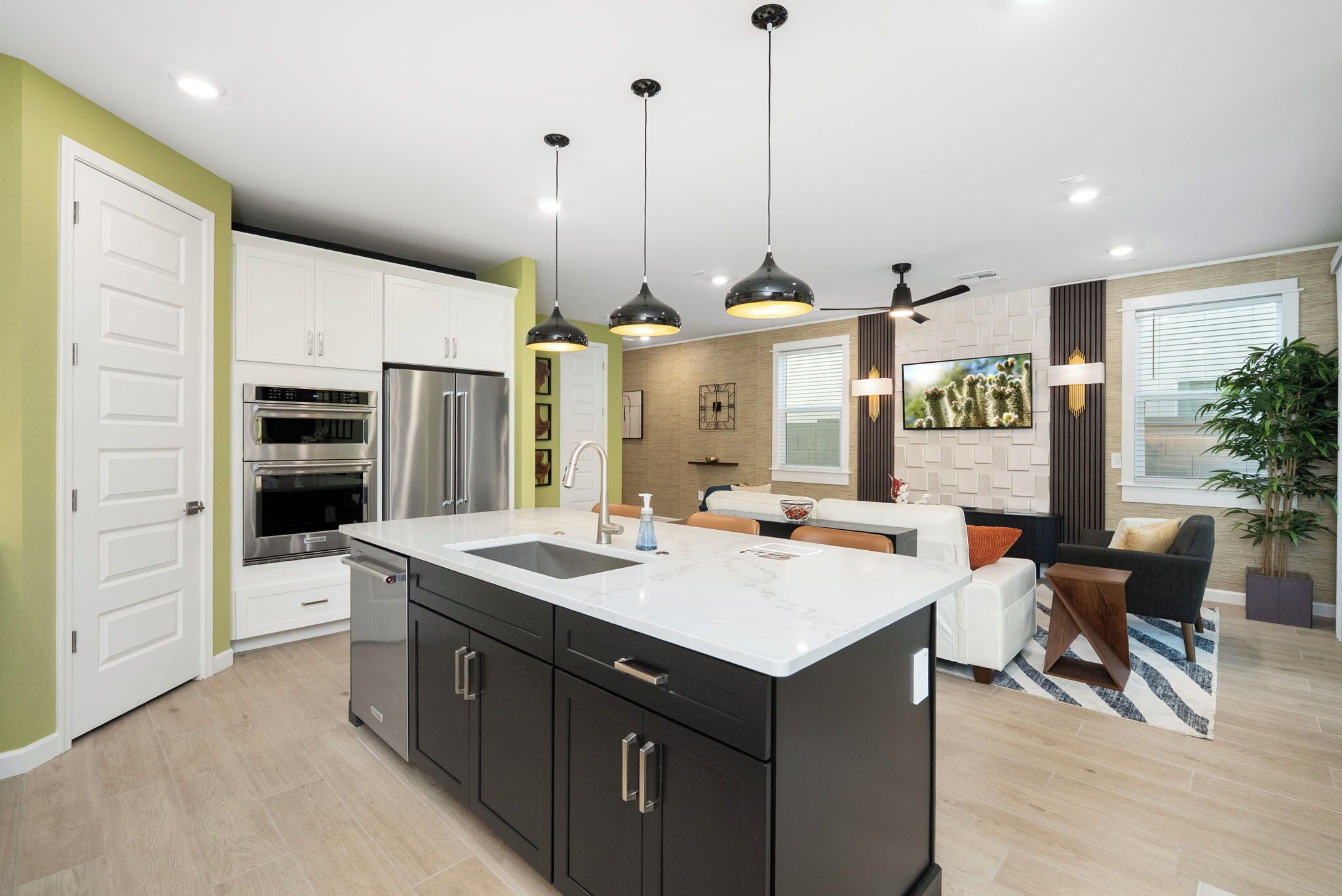 A modern kitchen with a central island, built-in appliances, pendant lighting, and a dining area with a sofa and coffee table.