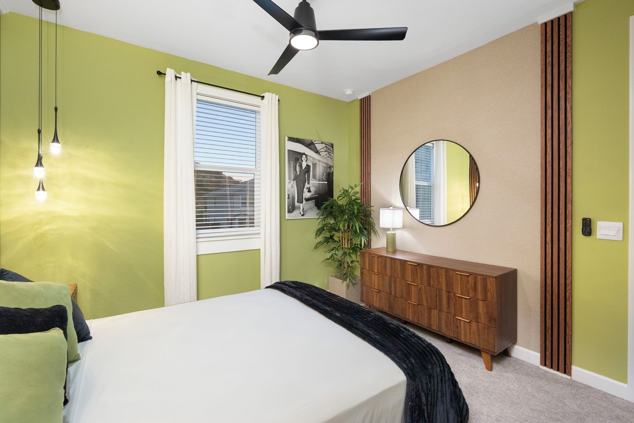 A bedroom with a bed, a ceiling fan, a dresser, a mirror, and a window with blinds.