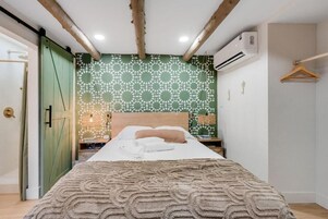 Un dormitorio con una cama, pared de color verde con estampado, techo de madera y lámpara colgante.