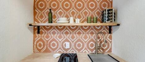 Uma cozinha com painel decorativo atrás do fogão, bancada de madeira, pia e fogão.