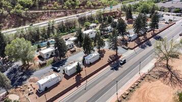 Vista aérea de um camping com veículos recreativos estacionados ao longo de uma estrada, cercado por árvores e uma trilha de terra.