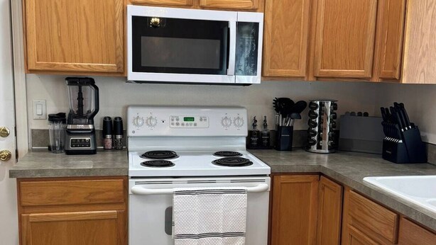 A kitchen with wooden cabinets, a white stove, a microwave, and a coffee maker. - Quiet Home Near Everything (Hermiston)