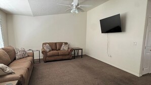 A living room with a brown sofa, a small table, a ceiling fan, and a mounted TV. - Quiet Home Near Everything (Hermiston)